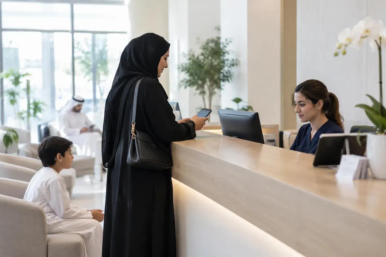 An Emirati woman in an abaya checks in at the bright reception of a private clinic on Al Wasl Road, Dubai, showing her phone to the receptionist while her son waits on a sofa.