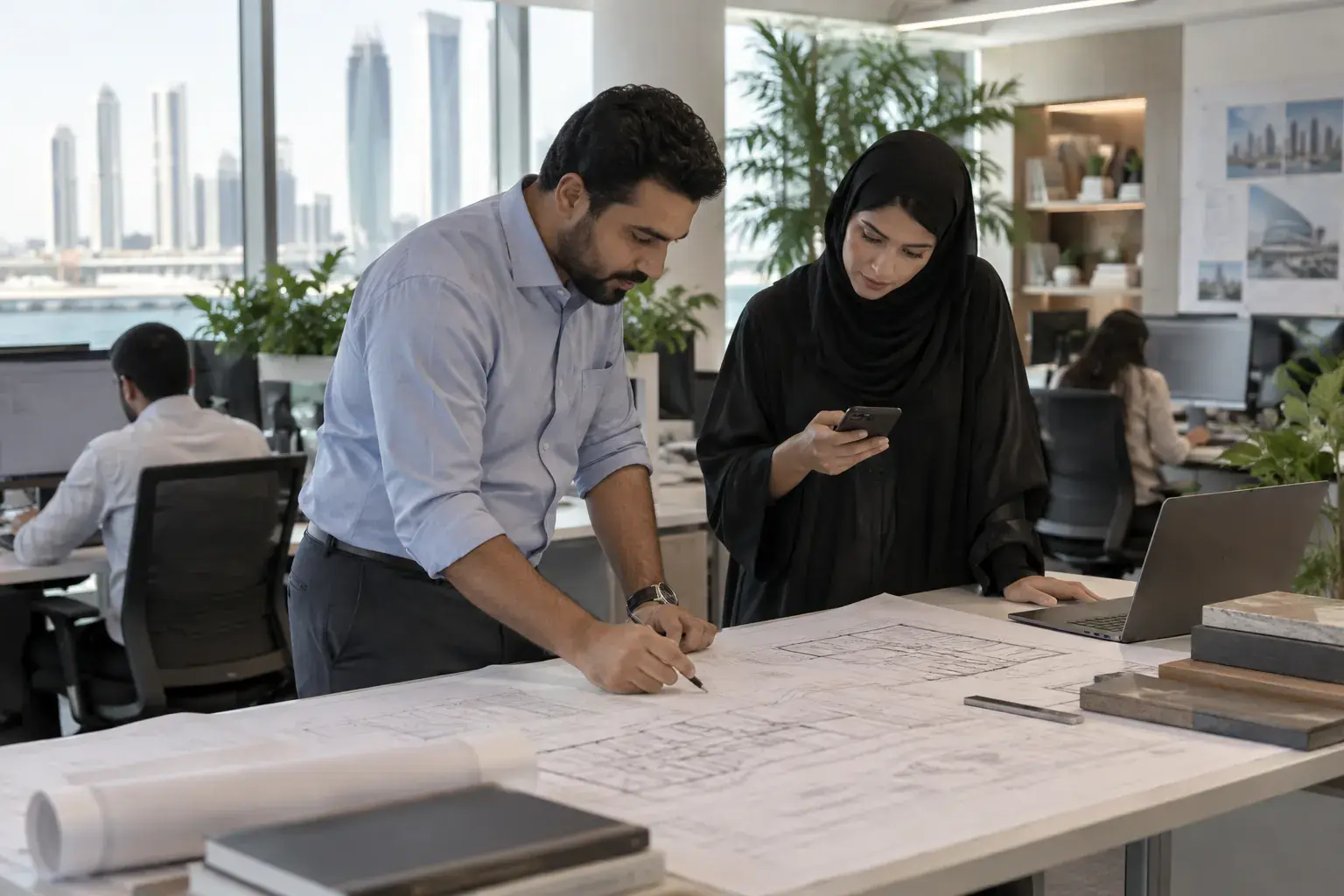 An MEP engineer and an architect lean over a large printed drawing at a standing desk in an Abu Dhabi consultancy studio, one marking it with a pen.
