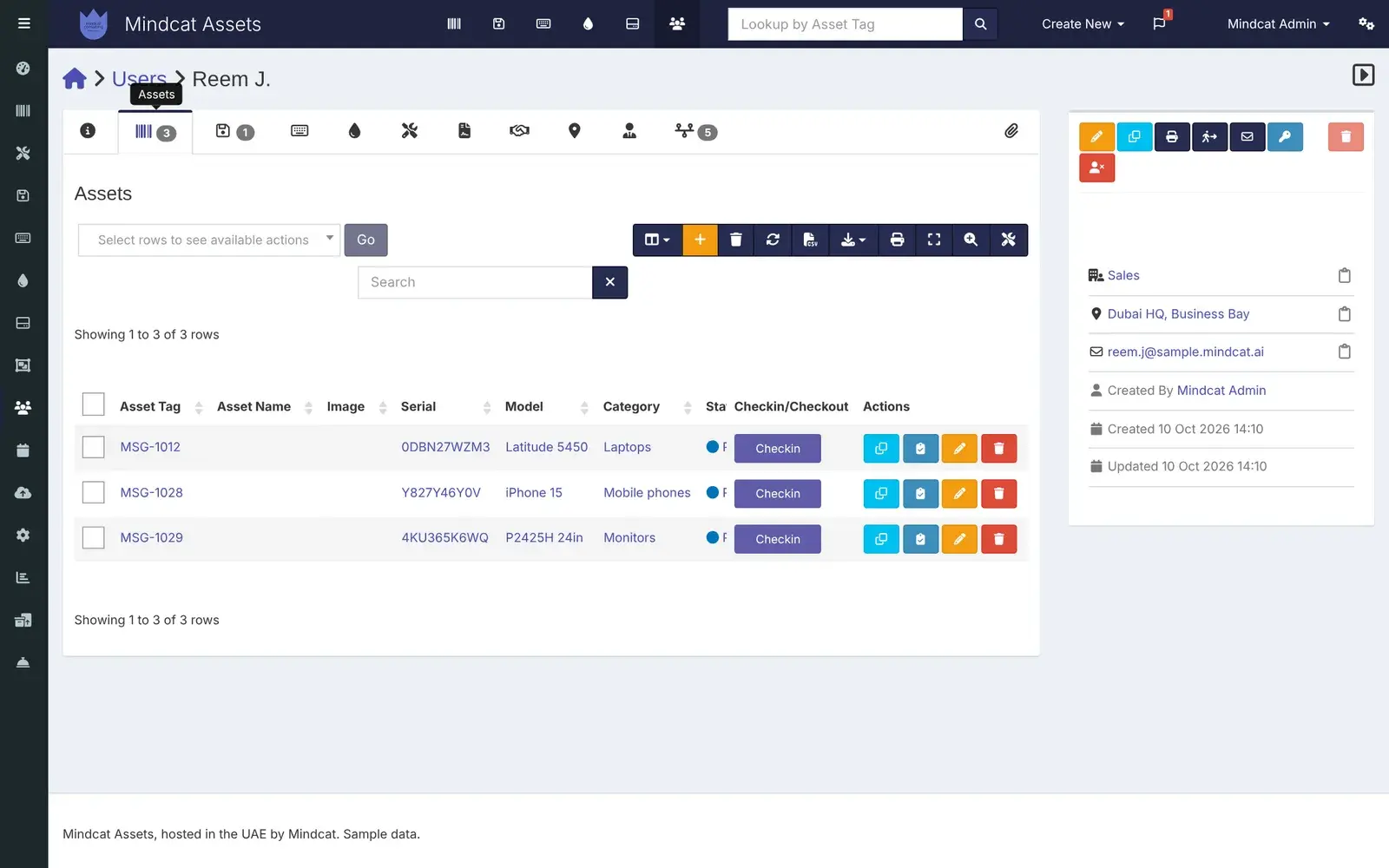 Mindcat Assets person record for Reem J. at Dubai HQ, Business Bay: the Assets tab with three items, MSG-1012 Latitude 5450, MSG-1028 iPhone 15 and MSG-1029 monitor, with serial numbers and check-in buttons.